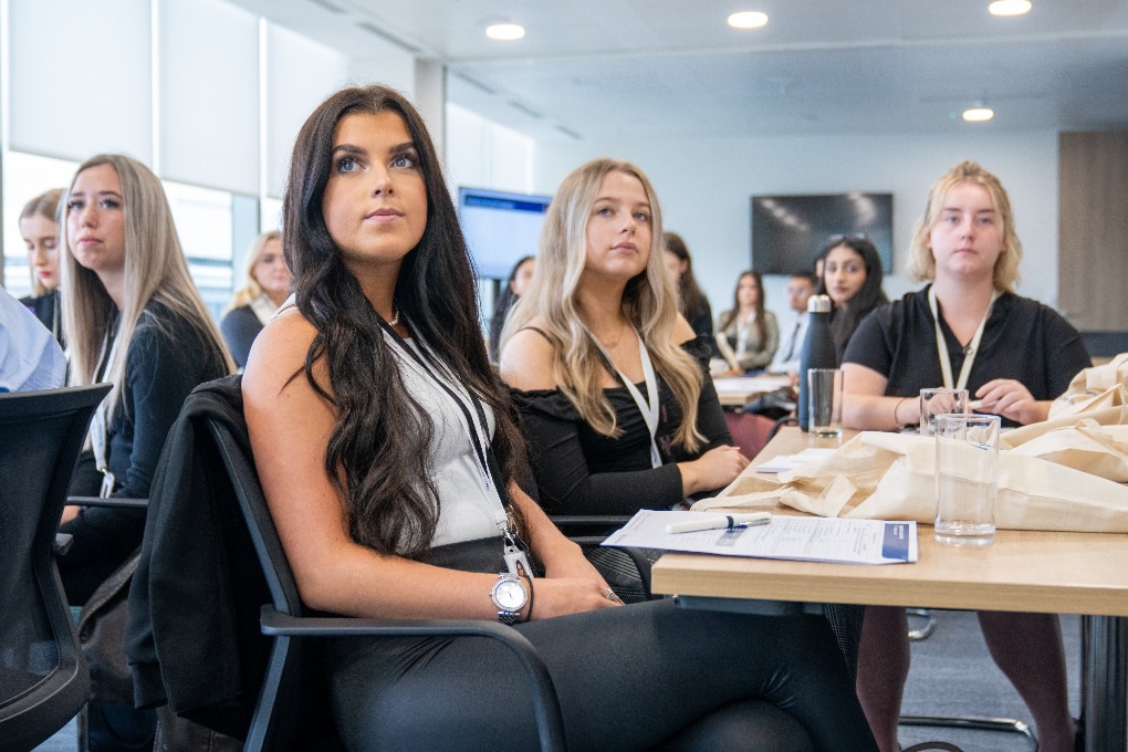 A group of apprentices sat at tables watching a presentation in an office